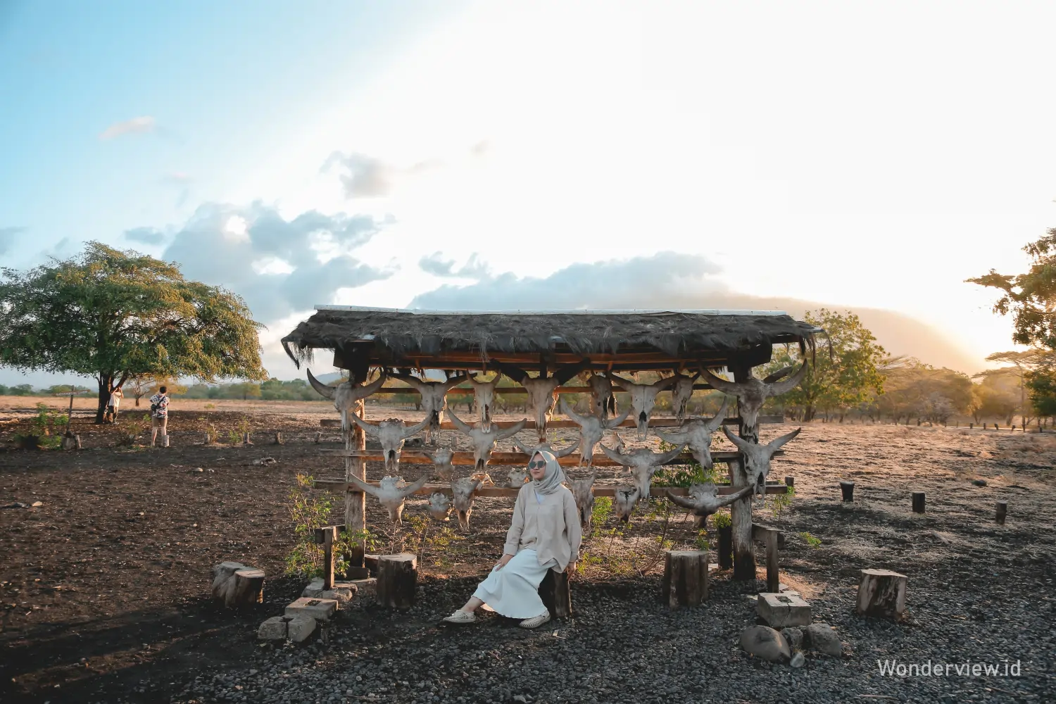 Wisatawan duduk di depan spot foto dekoratif di Taman Nasional Baluran saat matahari terbenam.