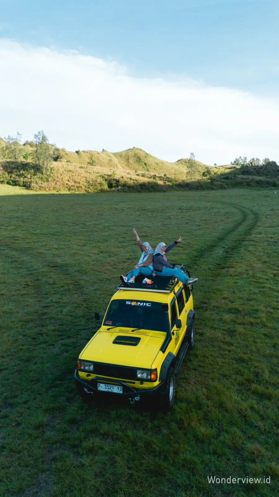 Dua wisatawan duduk di atas jeep kuning sambil menikmati pemandangan savana luas di Kawah Wurung Banyuwangi.