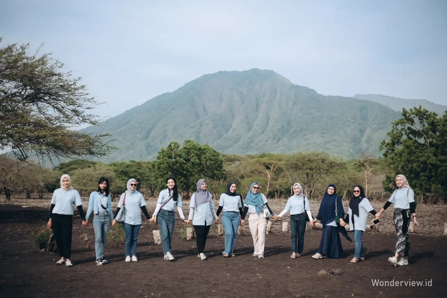 Rombongan wisatawan berdiri berpegangan tangan di savana Taman Nasional Baluran dengan latar Gunung Baluran.