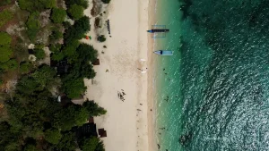 Pemandangan udara Pulau Tabuhan yang menampilkan pasir putih, perahu berlabuh, dan gradasi air laut berwarna turkis hingga biru tua.