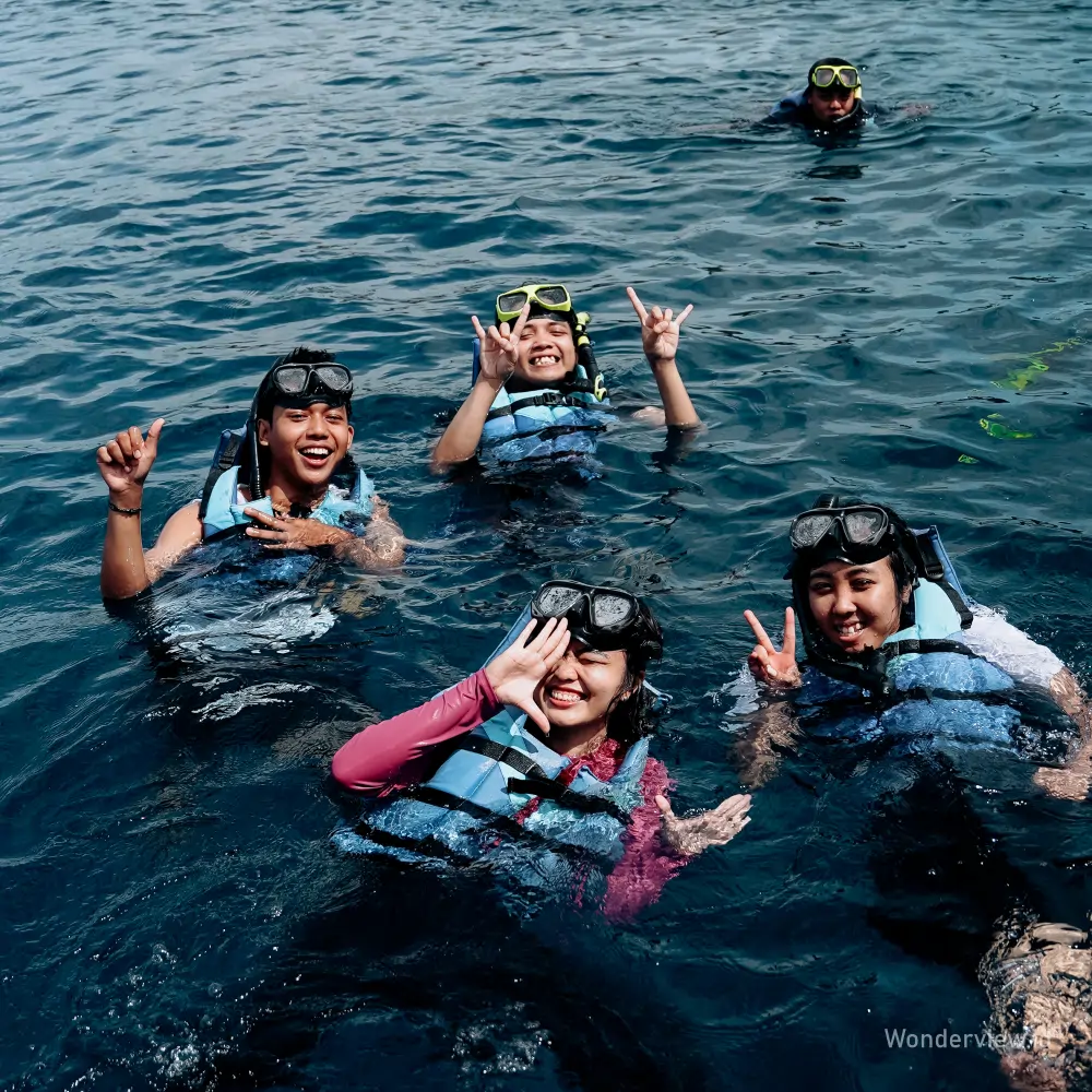 Empat wisatawan snorkeling sambil tersenyum dan melambaikan tangan di perairan Bangsring Banyuwangi.